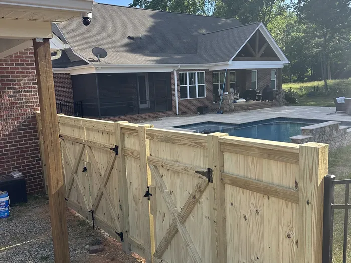 A braced wooden gate and its post line set in a back yard with the ground still open