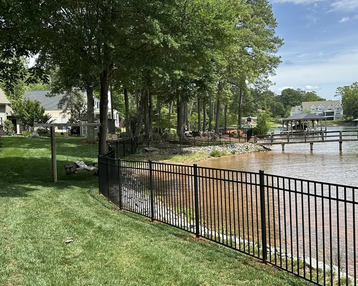 Black aluminum fence along a Lake Norman shoreline with a dock behind it