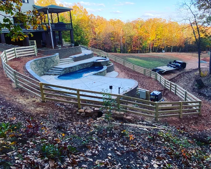 Four board ranch rail around a pool deck with autumn woods behind