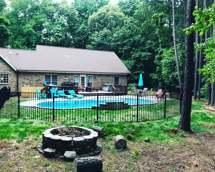 Black aluminum fence enclosing a pool and fire pit in a wooded back yard